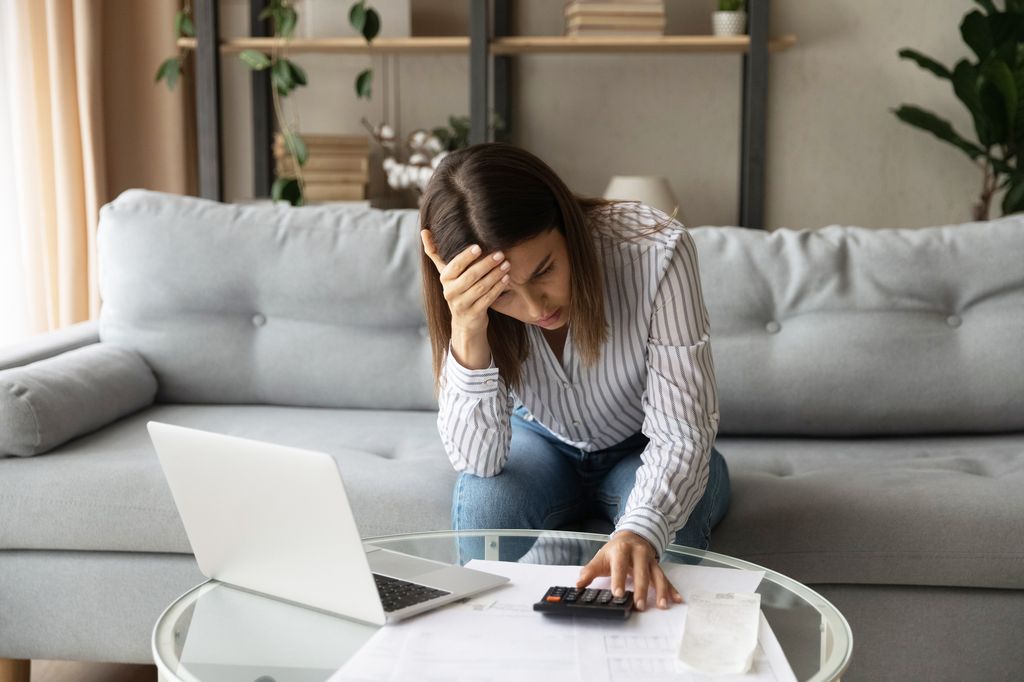 Woman looking stressed looking at a calculator while sitting on a sofa