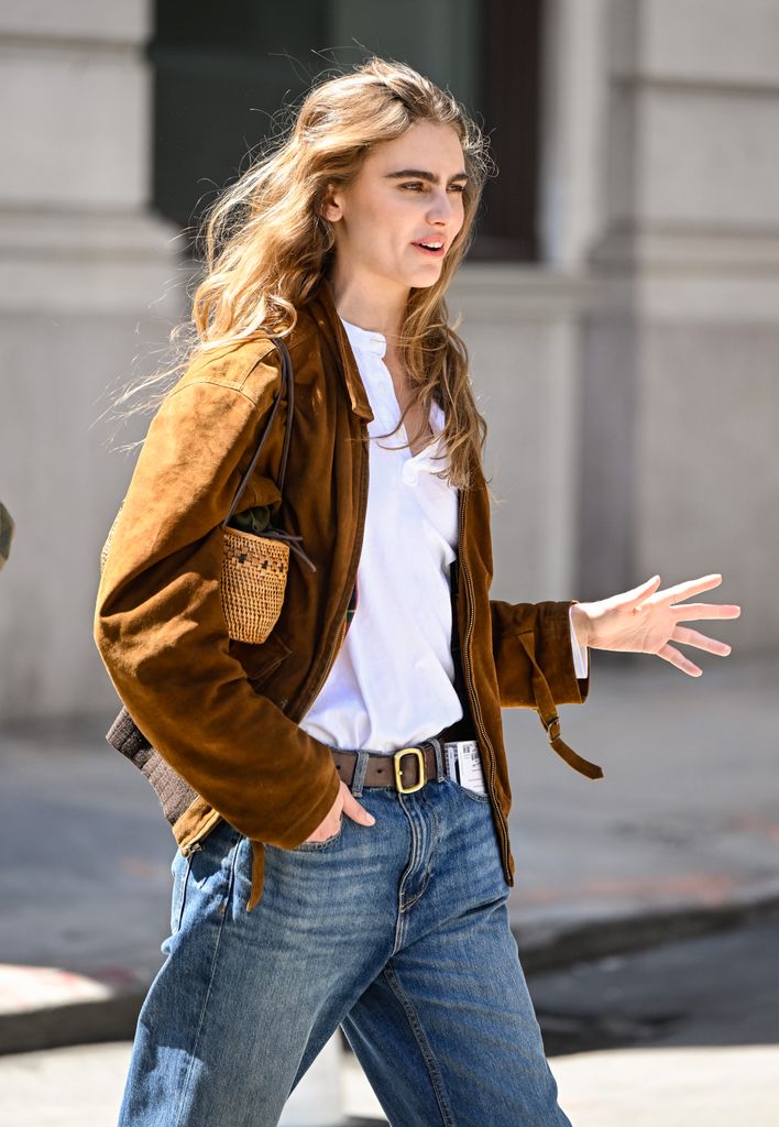 Model Mia Armstrong is seen wearing a brown jacket, white top, blue jeans, brown and gold buckle belt