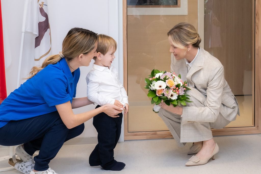 Princess Charlene kneels down whilst holding a boquet of flowers