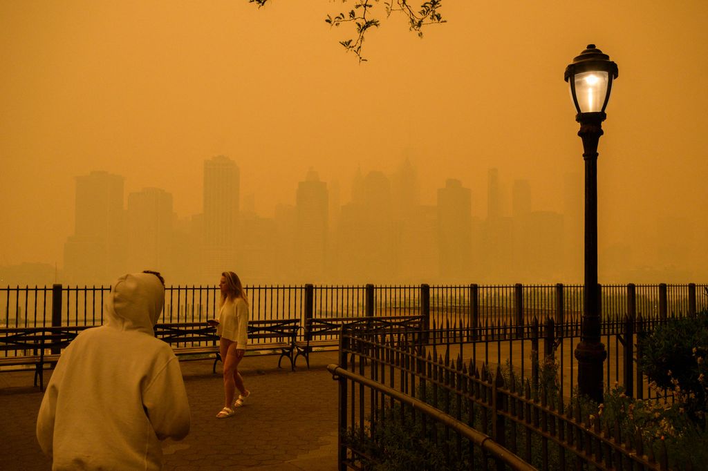 The skyline of lower Manhattan is seen past pedestrians as smoke from wildfires in Canada cause hazy conditions in New York City on June 7, 2023. An orange-tinged smog caused by Canada's wildfires shrouded New York on Wednesday, obscuring its famous skysc