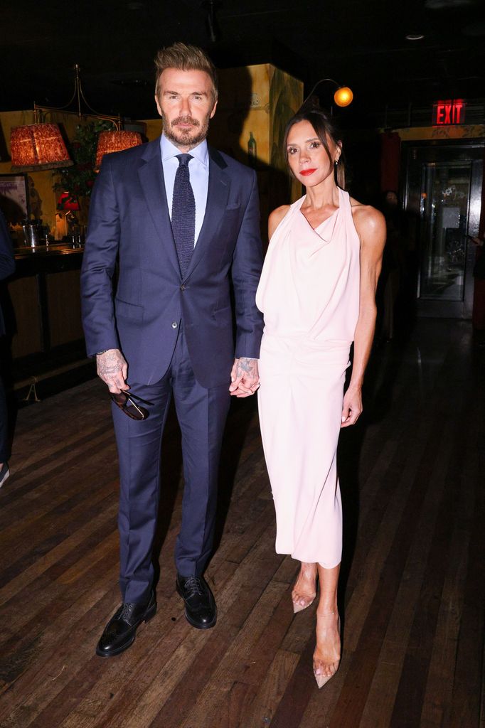 Victoria Beckham em vestido branco com lábios vermelhos ao lado de David