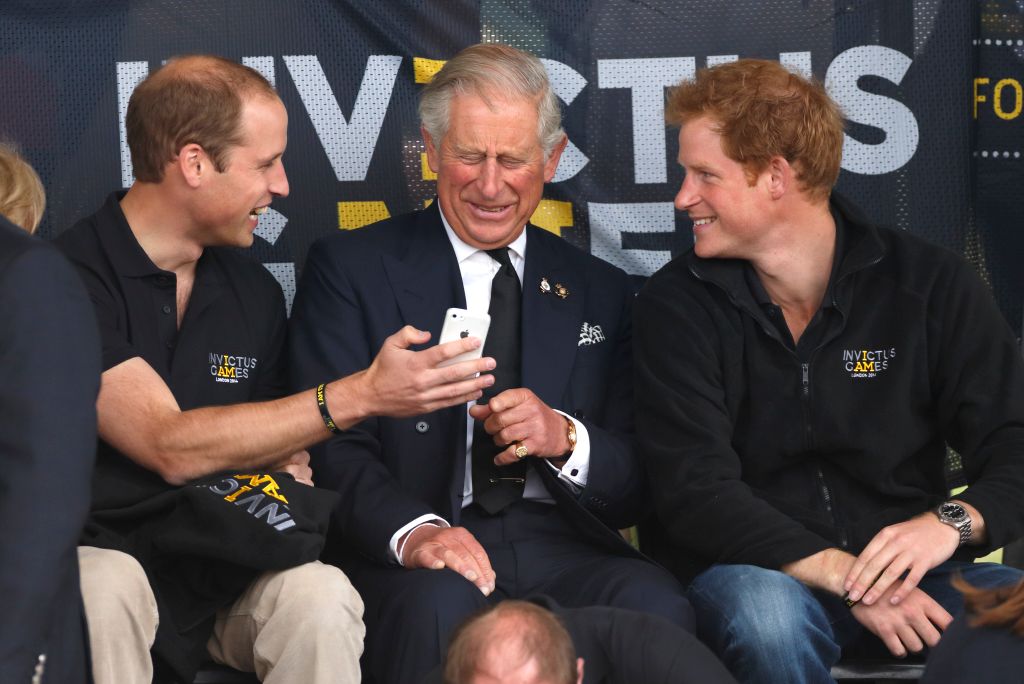 Prince William, Duke of Cambridge, Prince Charles, Prince of Wales & Prince Harry look at a mobile phone as they watch the athletics during the Invictus Games