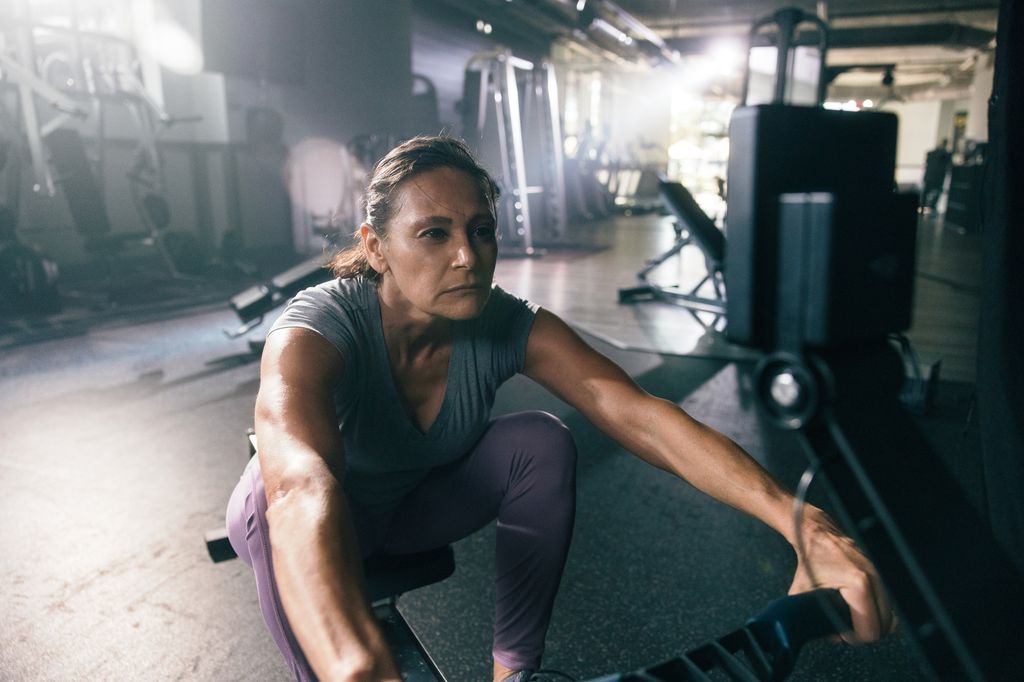 A woman struggles to use rowing machine in a gym in the morning.