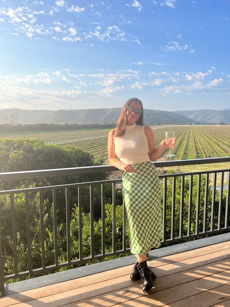 woman standing with a glass of wine against a backdrop of fields