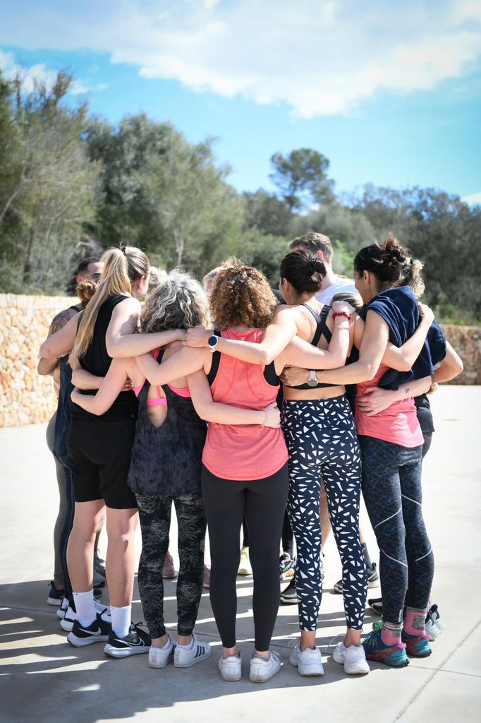 group of women hugging outside in the sun wearing workout clothes