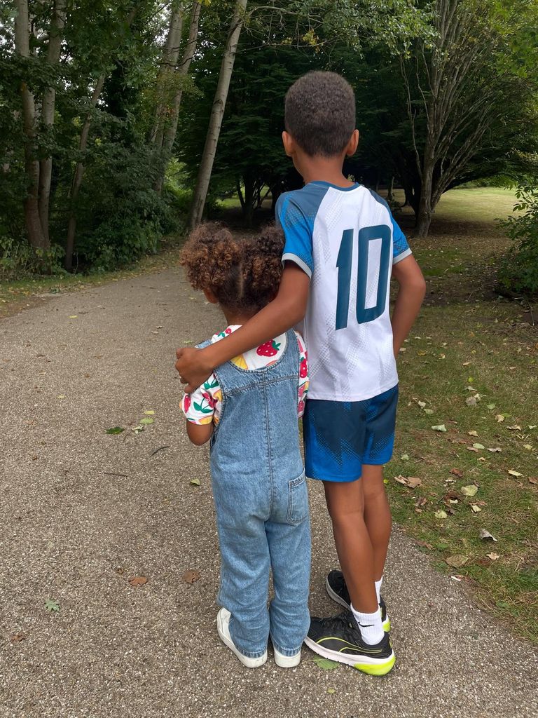 boy with arm around little girl from behind in woodland