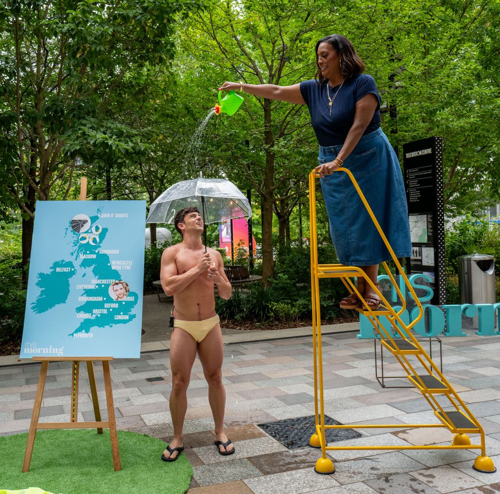 Alison Hammond on a ladder pouring a watering can over Tom Daley - he holds an umbrella and stands in yellow Speedos