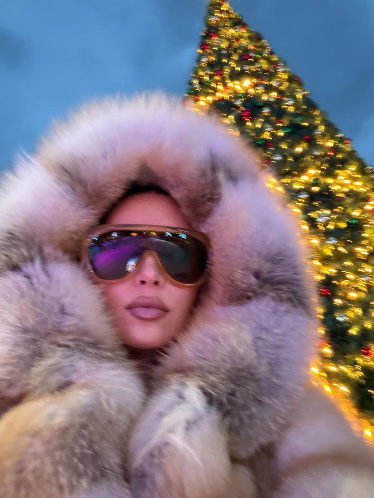 Kim Kardashian poses in front of a Christmas Tree in a fluffy hooded coat 