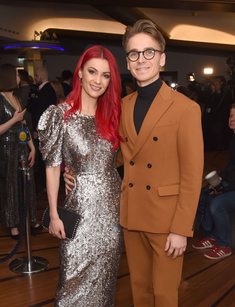 Dianne Buswell in a silver dress standing with Joe Sugg in a chocolate-coloured suit
