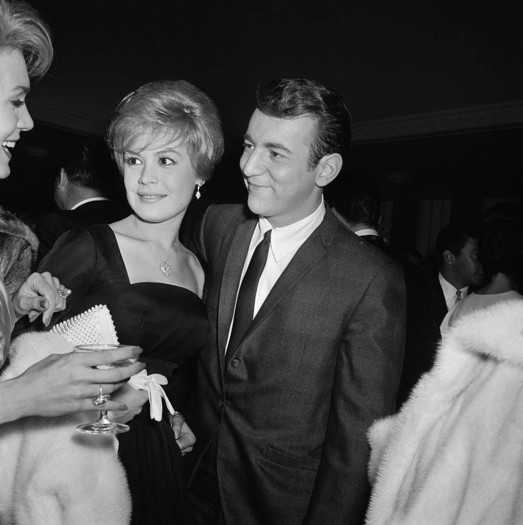 Bobby Darin et Sandra Dee se tiennent l'un à côté de l'autre et regardent tous deux leur ami avec des sourires.