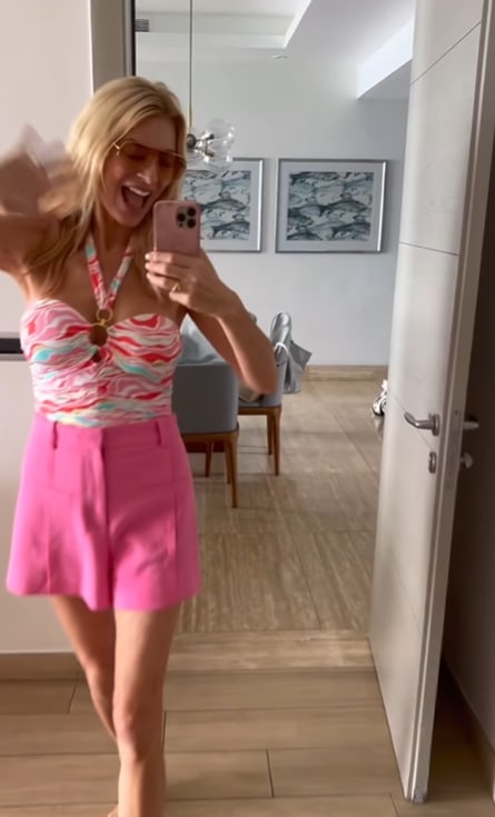 Tess in mirror selfie waving in a pink swimsuit