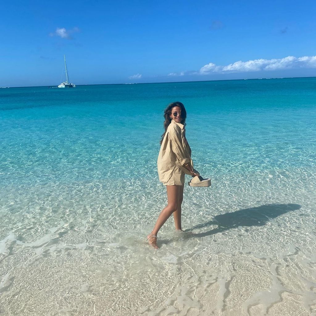 Michelle Keegan in sea in beige shirt holding sandals