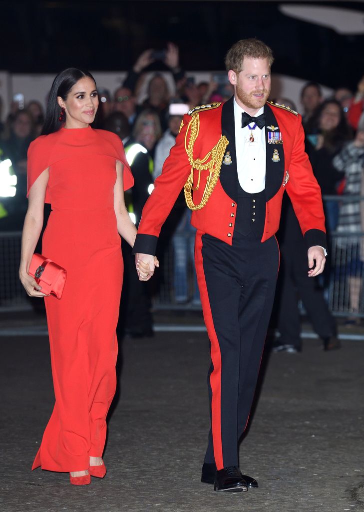 Prince Harry in red jacket and Meghan in red caped dress