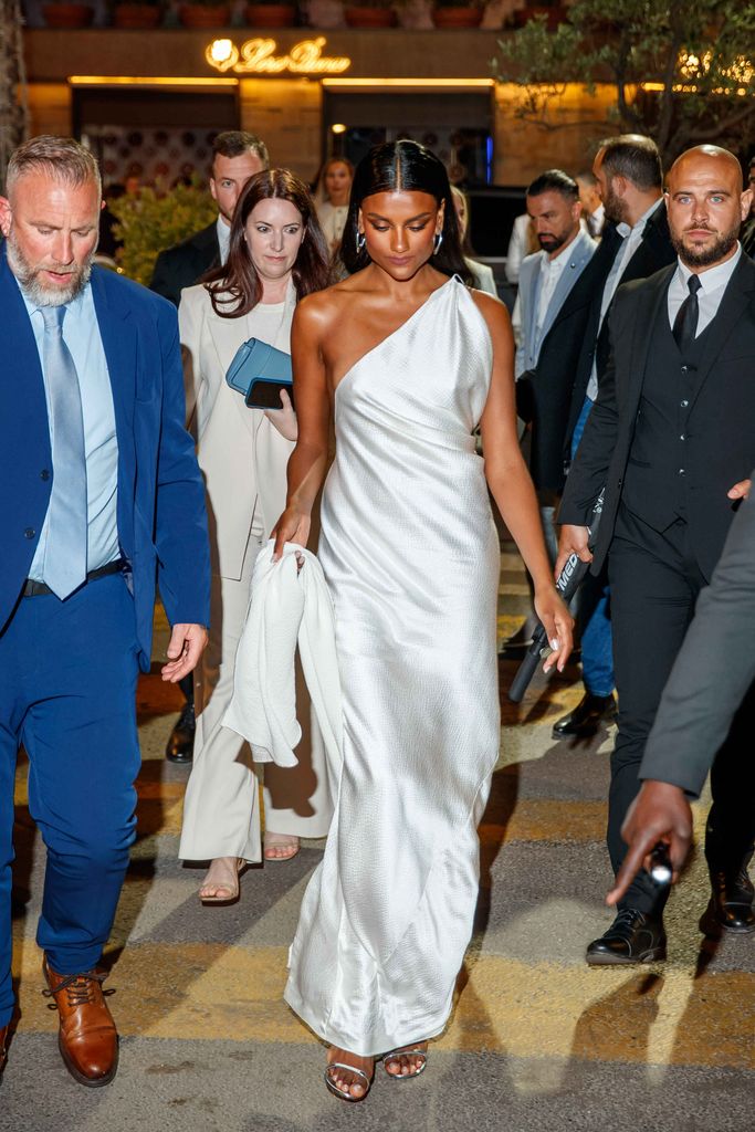 Simone Ashley holding the bottom of her white dress as she walks