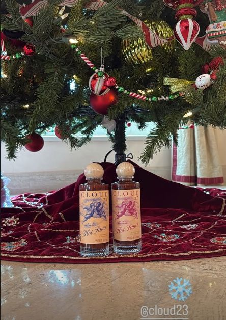 Two bottles of fragrance underneath a decorated Christmas tree