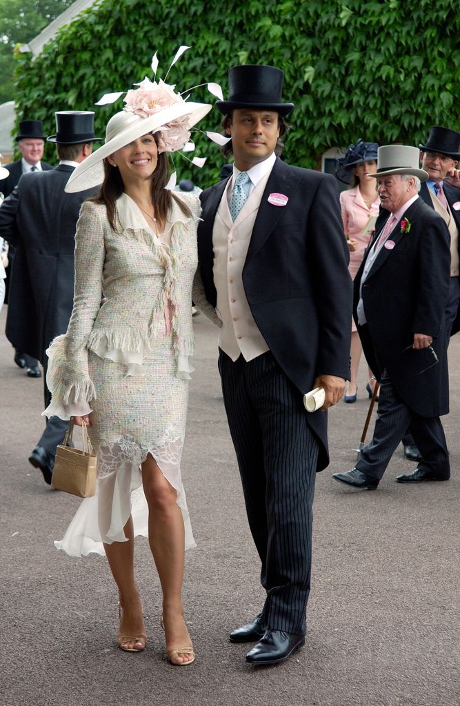 Elizabeth Hurley in a pastel tweed & chiffon skirt suit and oversized floral hat at Royal Ascot standing next to  Arun Nayar 