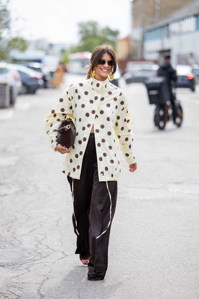 7: A guest wears dots print beige blouse, brown bag, pants outside Marimekko during Copenhagen Fashion Week day four on August 07, 2025 in Copenhagen, Denmark.