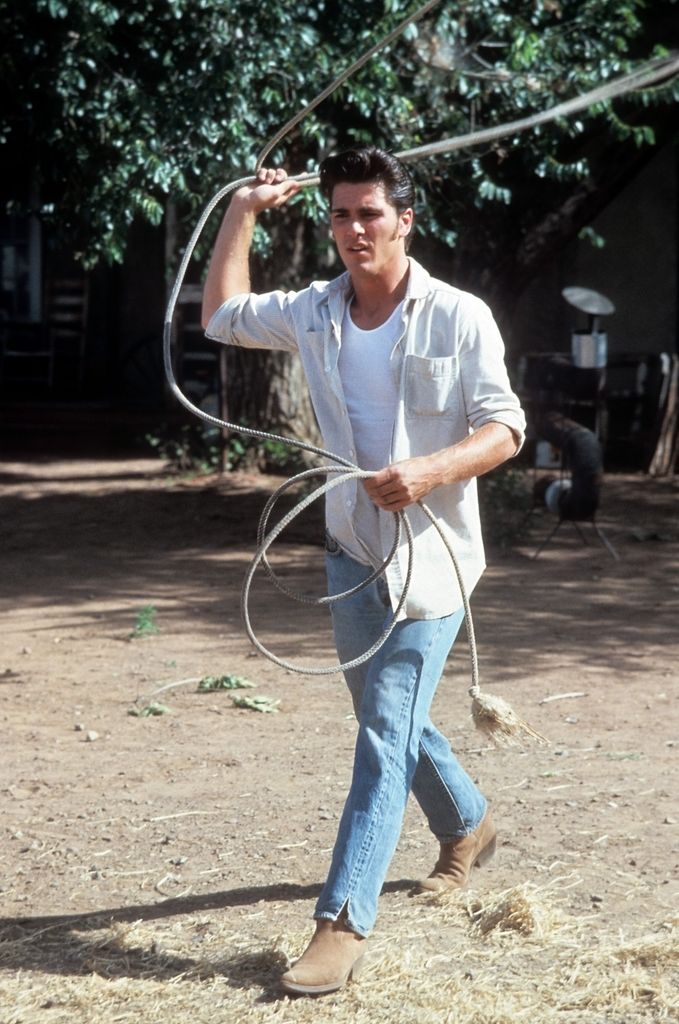 Michael Schoeffling tient un lasso dans les airs et avance à grands pas sur un sol poussiéreux.