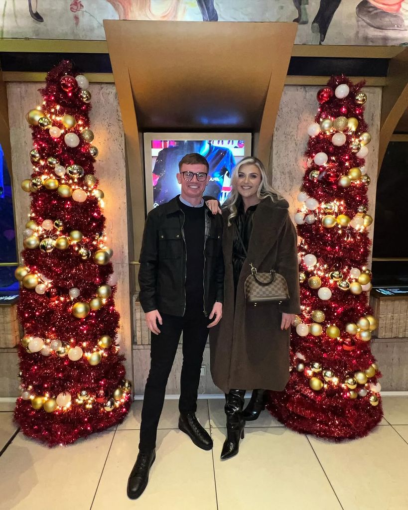 Izzi Warner and guest standing in front of two Christmas trees