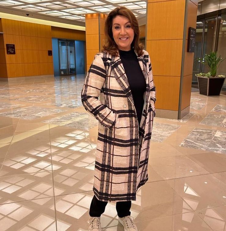 Jane McDonald in plaid coat standing in hotel foyer