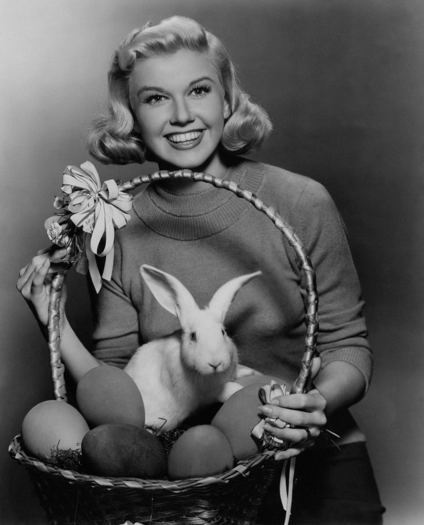 Doris Day in a sweater holds a basket filled with a rabbit and Easter eggs.