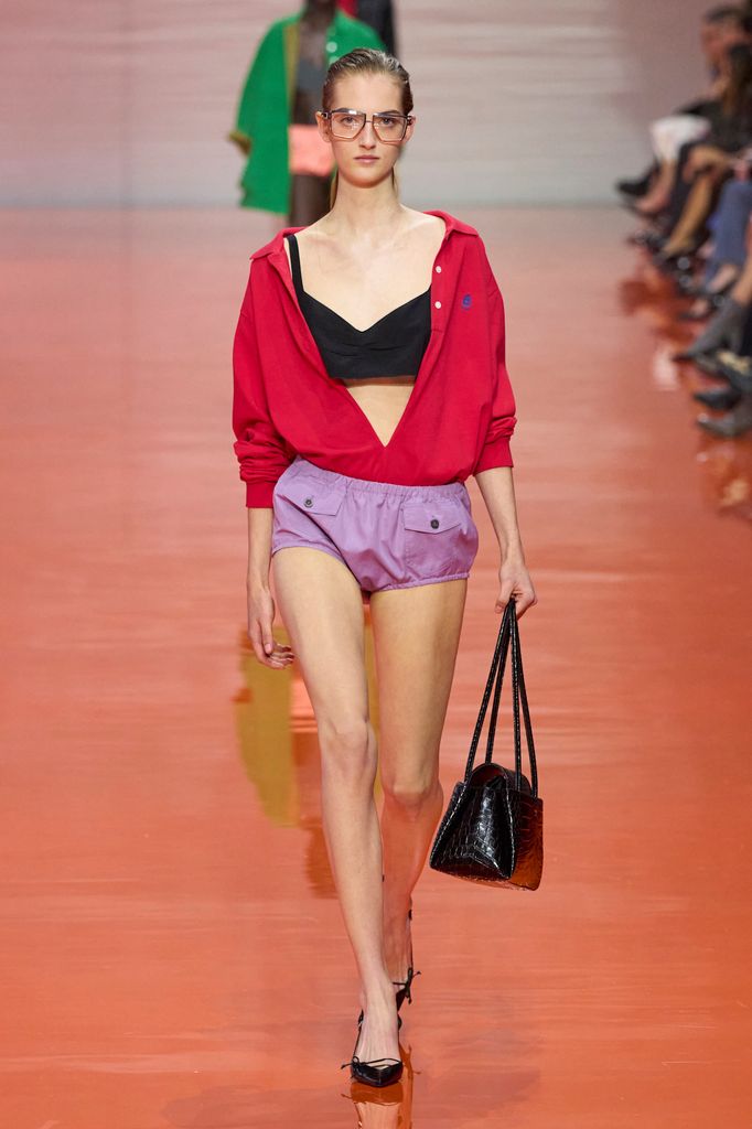 A model wears a bright red shirt undone over a dark brown crop top, teamed with lilac bloomers. 