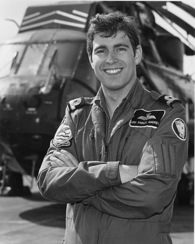 Black-and-white photo of Prince Andrew with his arms crossed in front of a helicopter