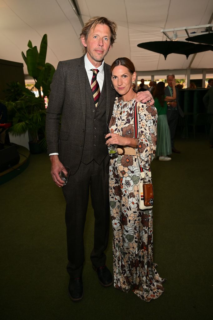 Andy Cato in a brown tweed three-piece suit and a woman in a floral maxi dress pose together at the RHS Chelsea Flower Show 2025