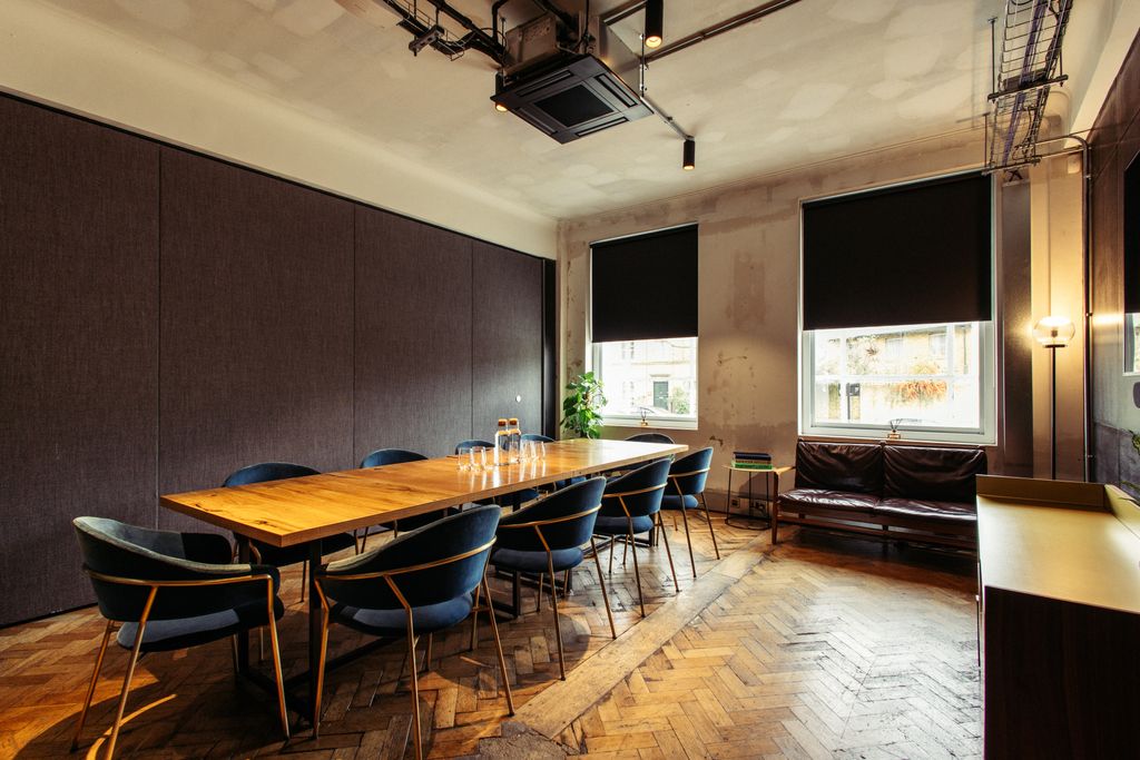 The drawing room in The Ministry with soft yellow lighting, a wooden table in the centre and blue chairs