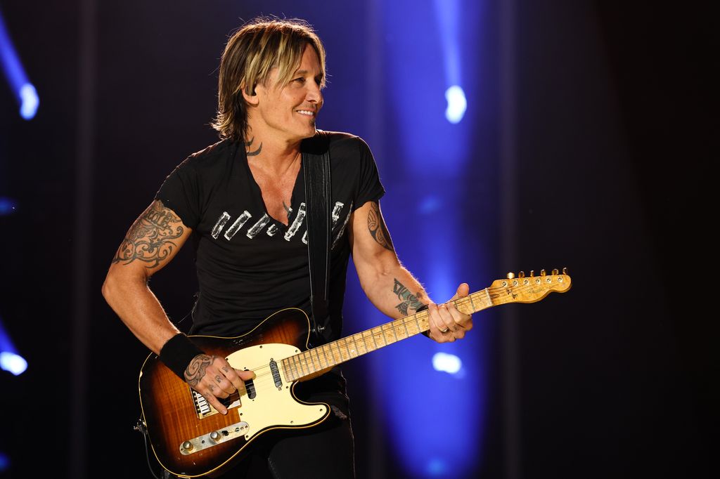 Keith Urban performing on stage with a guitar, looking to the right