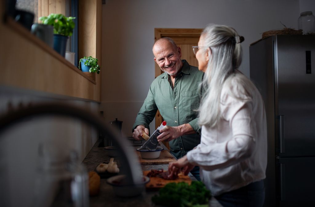 Senior couple preparing meal, cutting vegetable and cooking together in their kitchen.