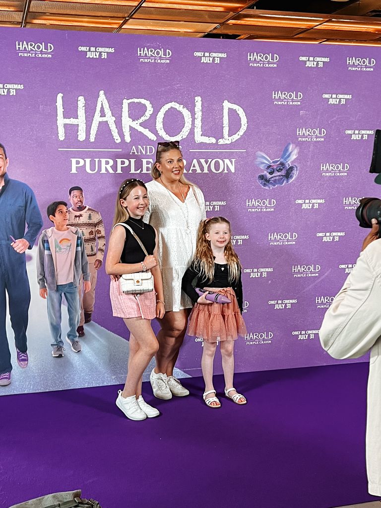 woman posing on a purple carpet for a film premiere with her two daughters