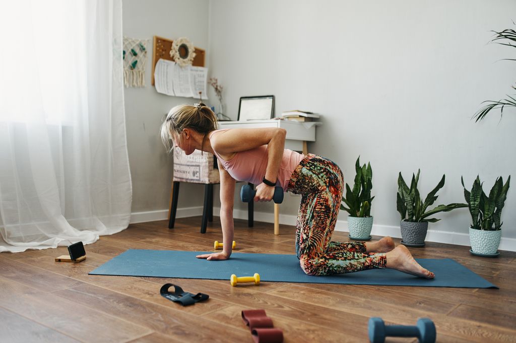 A young woman in a tracksuit is doing home fitness in a living room with green house flowers 