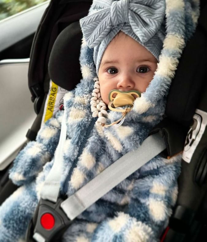 A baby in a snowsuit while strapped in a car seat