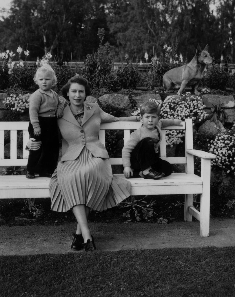 Queen Elizabeth sitting with her children, Charles and Anne and a royal corgi in the garden of Balmoral Castle in Scotland in 1952