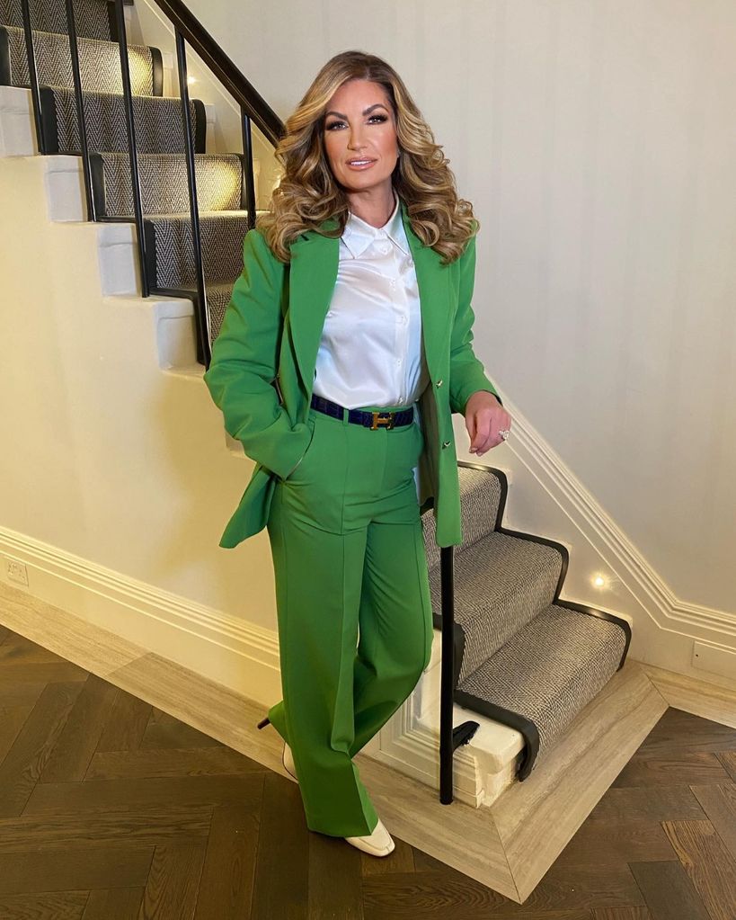 The Apprentice star Karren Brady wears a green suit and stands by the stairs