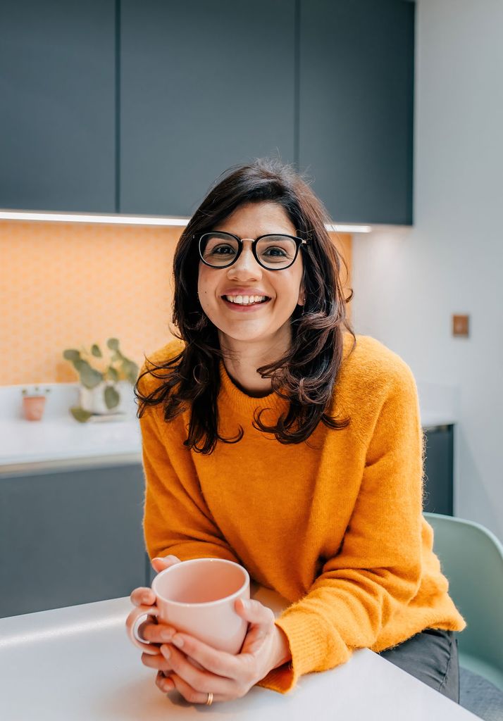 woman in orange jumper cradling cup in kitchen
