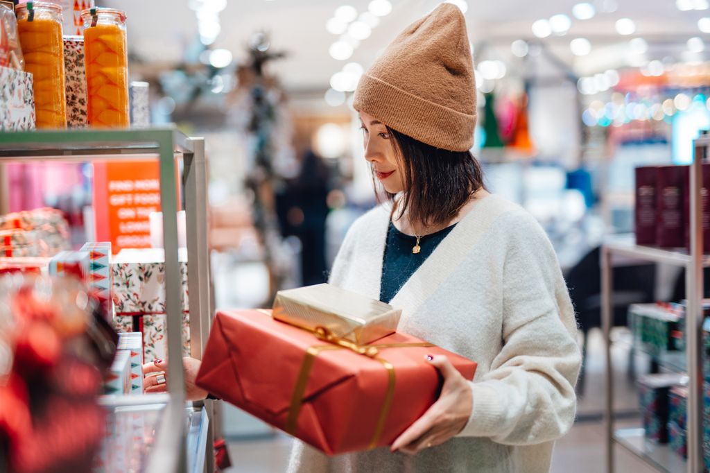 Beautiful young Asian woman choosing Christmas gifts from the store display in shopping mall. Christmas shopping.