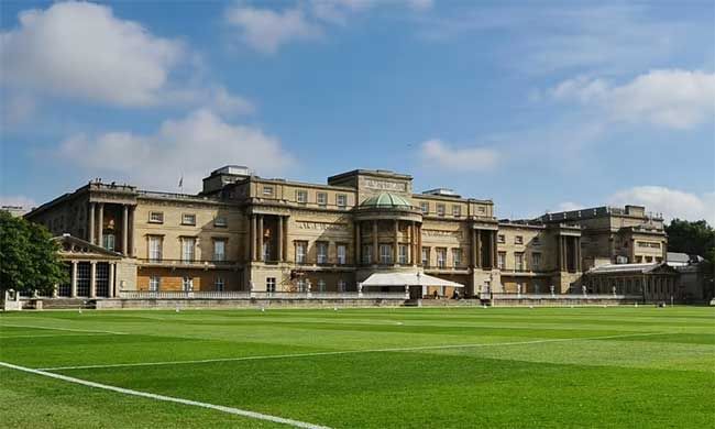 a rear view of Buckingham Palace in the distance across a large green lawn with a low wall running the width of the building