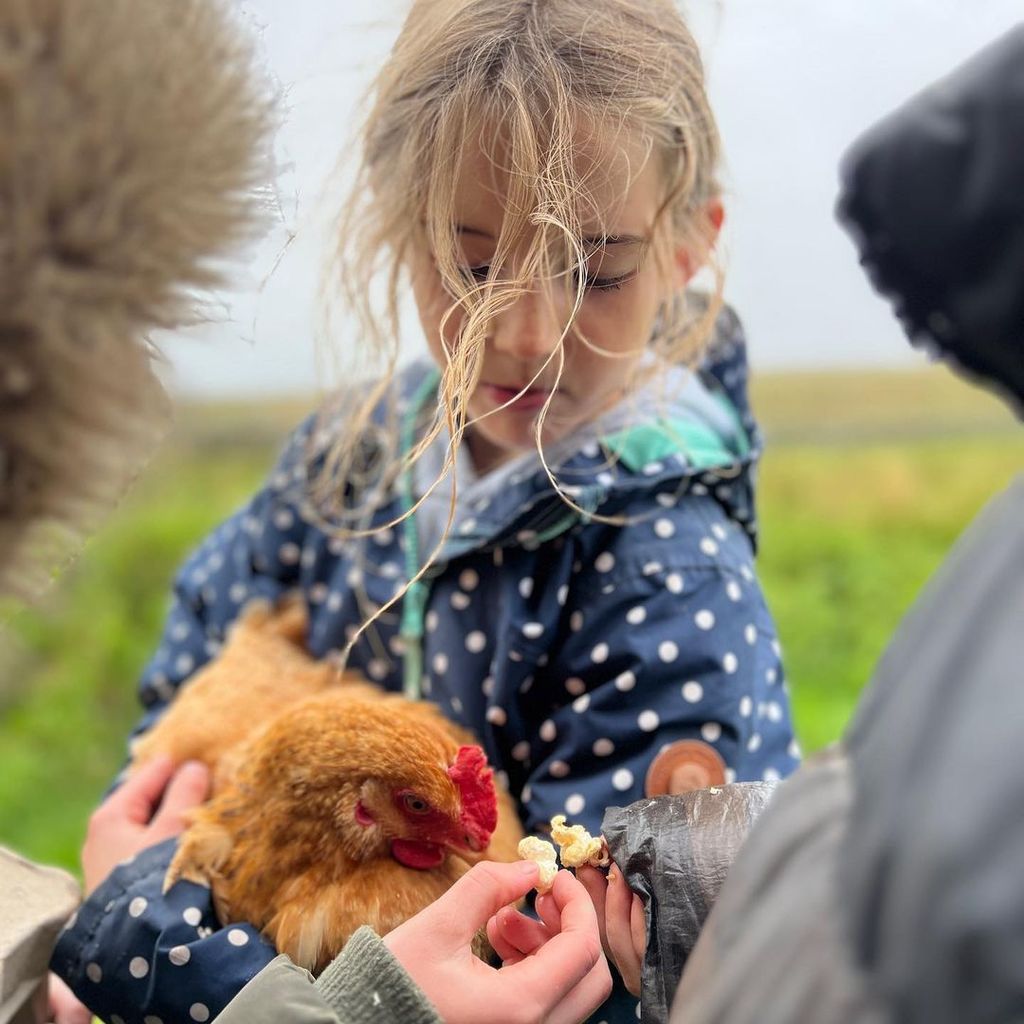 Amanda Owen's daughter with a chicken in a field