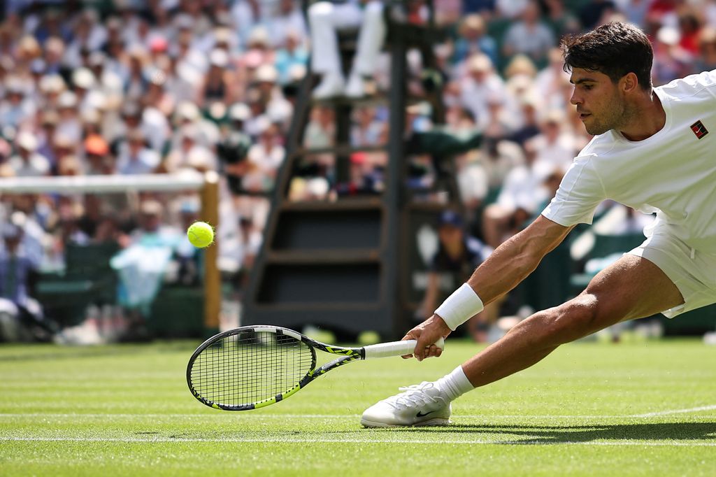 Carlos Alcaraz plays a backhand return to Italy's Fabio Fognini during their men's singles first round tennis match on the first day of the 2025 Wimbledon Championships at The All England Lawn Tennis and Croquet Club in Wimbledon, southwest London, on June 30, 2025