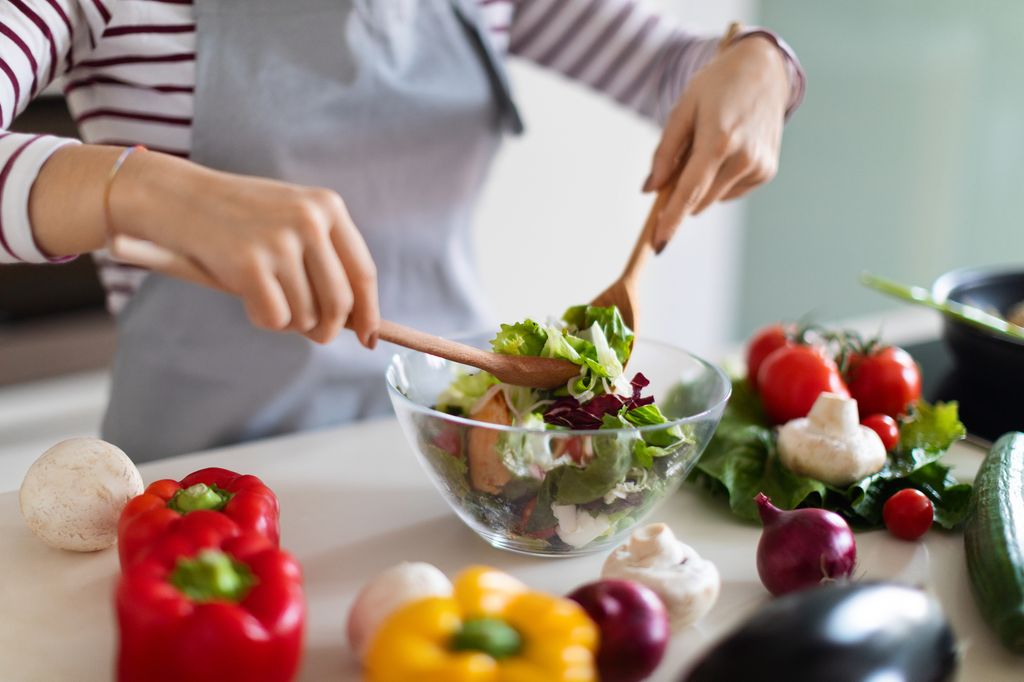 Concept de cuisine. Femme méconnaissable en chef de tablier gris faisant une salade de légumes biologiques frais, recadré de dame préparant de délicieux repas sains à la maison, mélangeant des légumes dans un bol, un gros plan, un espace de copie