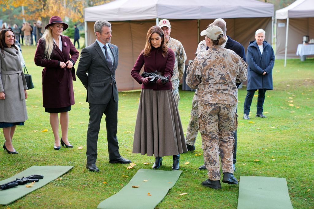 King Frederik X of Denmark (C-L) looks on as his wife Queen Mary of Denmark (C-R) holds a gun during their visit at Adazi Gymnasium in Adazi, Latvia, on October 29, 2025. During the visit, the Royal Couple observes civil defense education, which is a mandatory subject in secondary education. The Royal Couple is on a state visit to Latvia from October 28-29, 2025. The visit primarily focuses on international military cooperation, including visits to deployed Danish soldiers. (Photo by Ida Marie Odgaard / Ritzau Scanpix / AFP) / Denmark OUT (Photo by IDA MARIE ODGAARD/Ritzau Scanpix/AFP via Getty Images)          