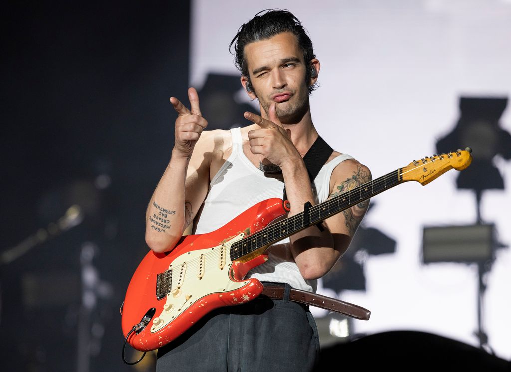 Matty Healy pointant sur scène avec une guitare rouge