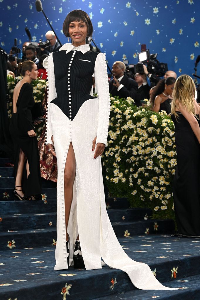 Zoe Saldana wears a white long sleeve sequin dress with black corset detail over the top of her torso.