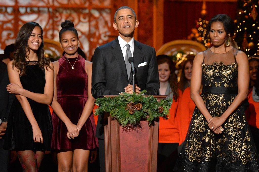 Barack Obama talking to a crowd with Michelle by his side and his daughters