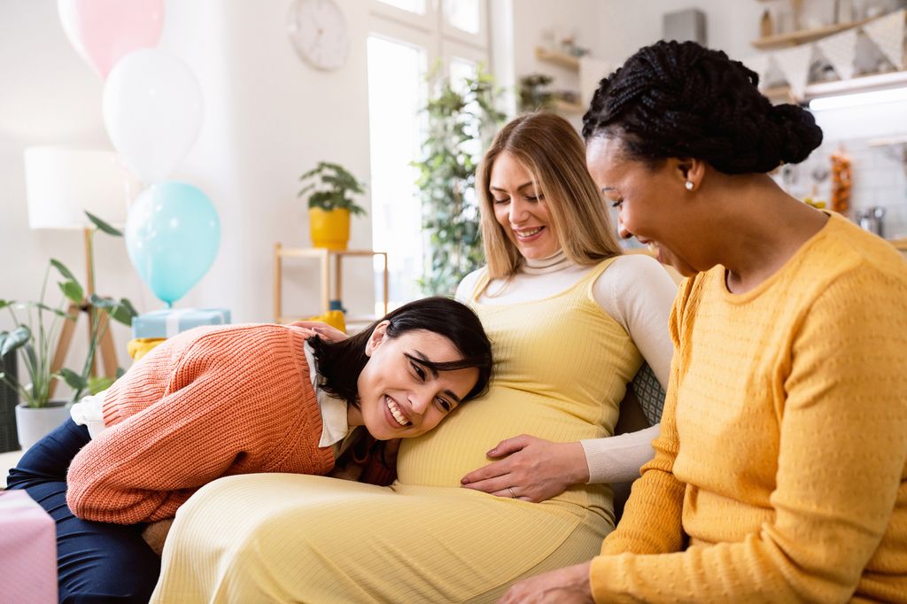 Caucasian woman leaning her head to pregnant belly of her friend, during her baby shower