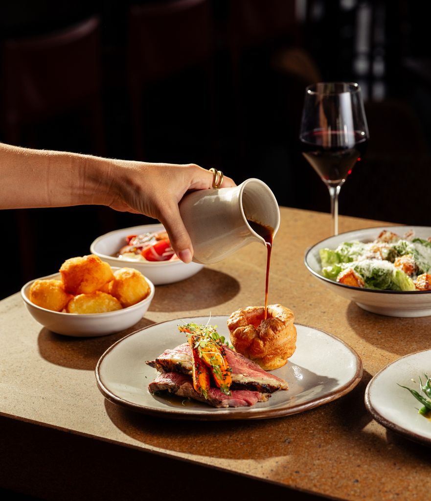 dinner plates on a table with a ladies hand pouring gravy over a roast dinner 