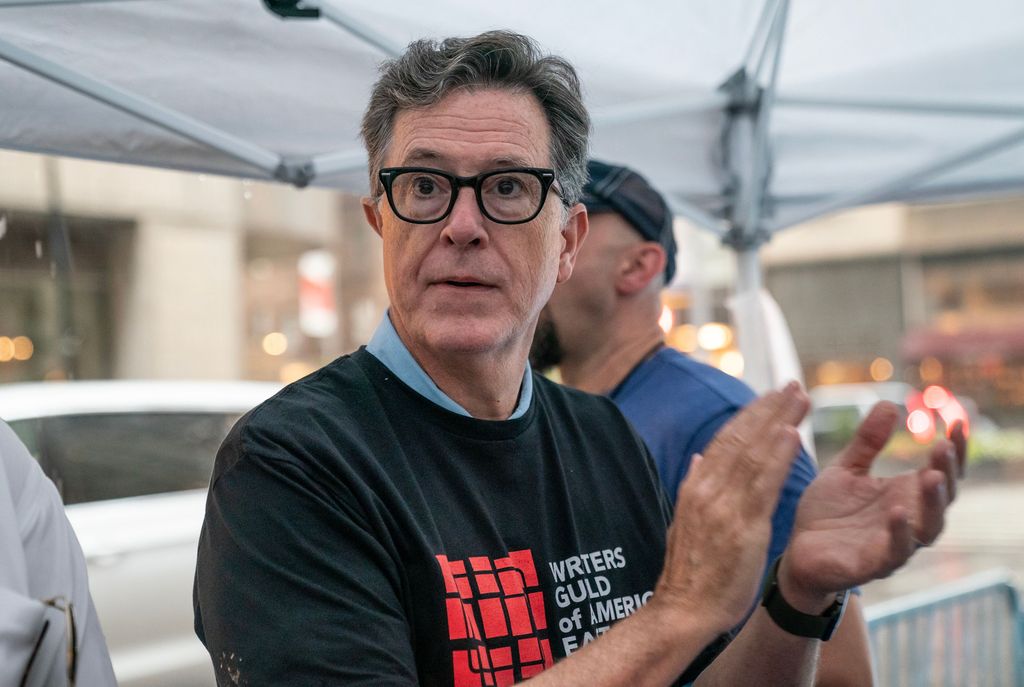 Stephen Colbert serves ice cream to striking members of Writers Guild of America picketing in front of Warner Brothers Discovery office, New York despite heavy rain
