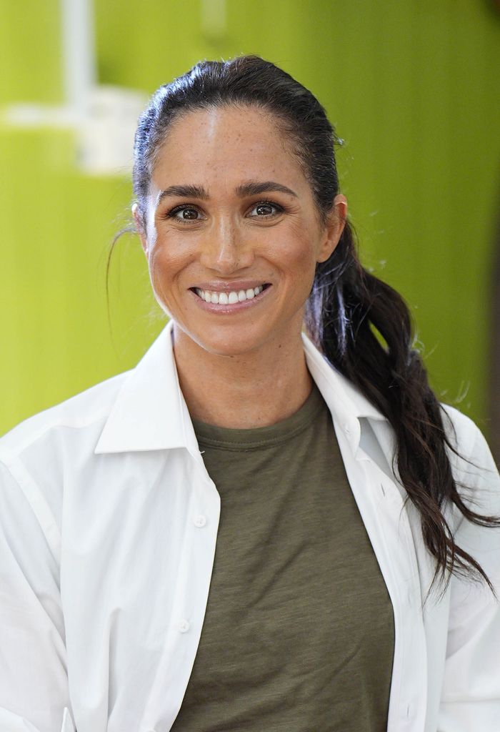La duchesse de Sussex souriante dans un t-shirt kaki et une chemise en lin blanc